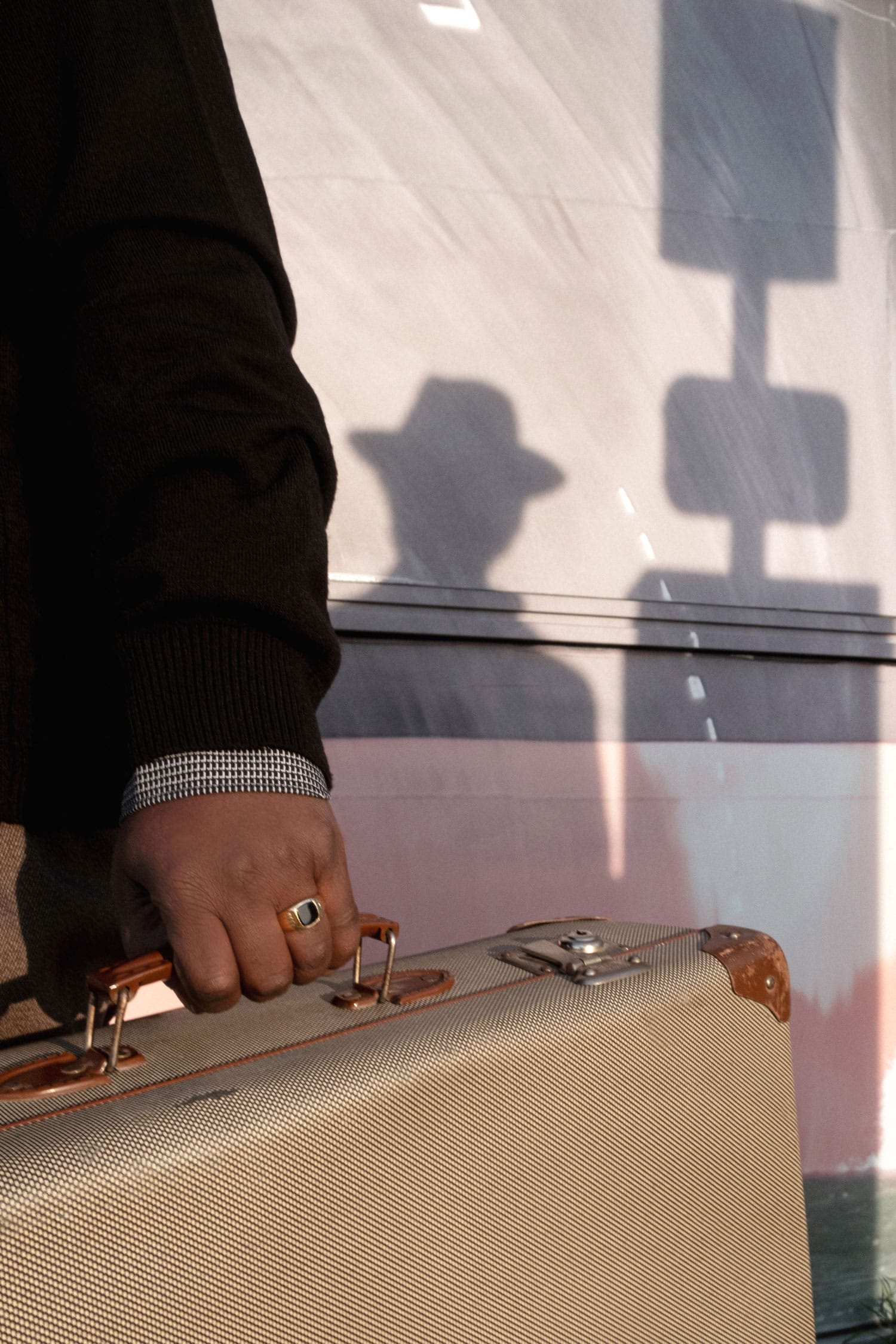 Photograph of a person holding a suitcase, its shadow reflected on the wall in the background