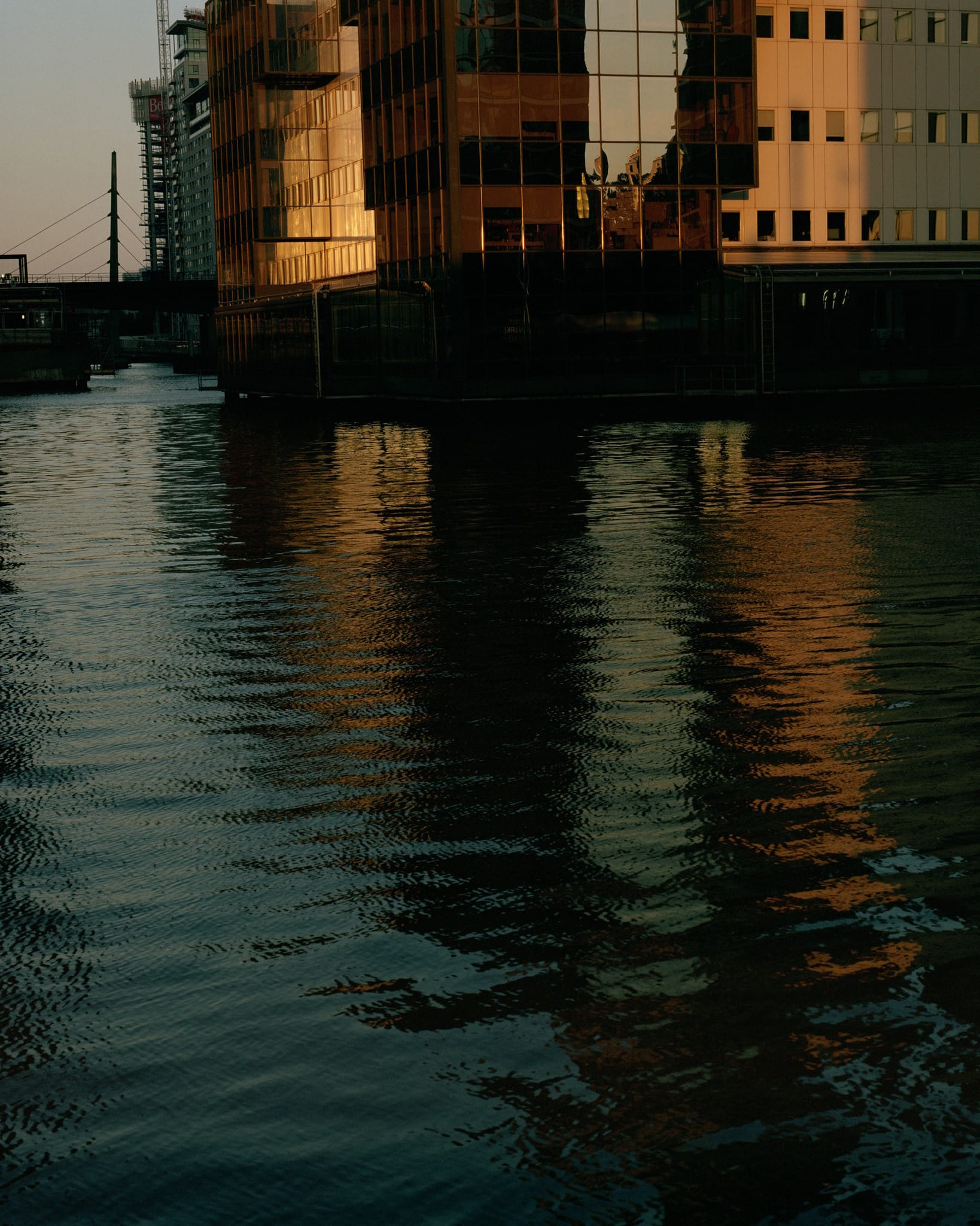 Photo in a urban port area with a large body of water in the foreground and skyscrapers in the background.