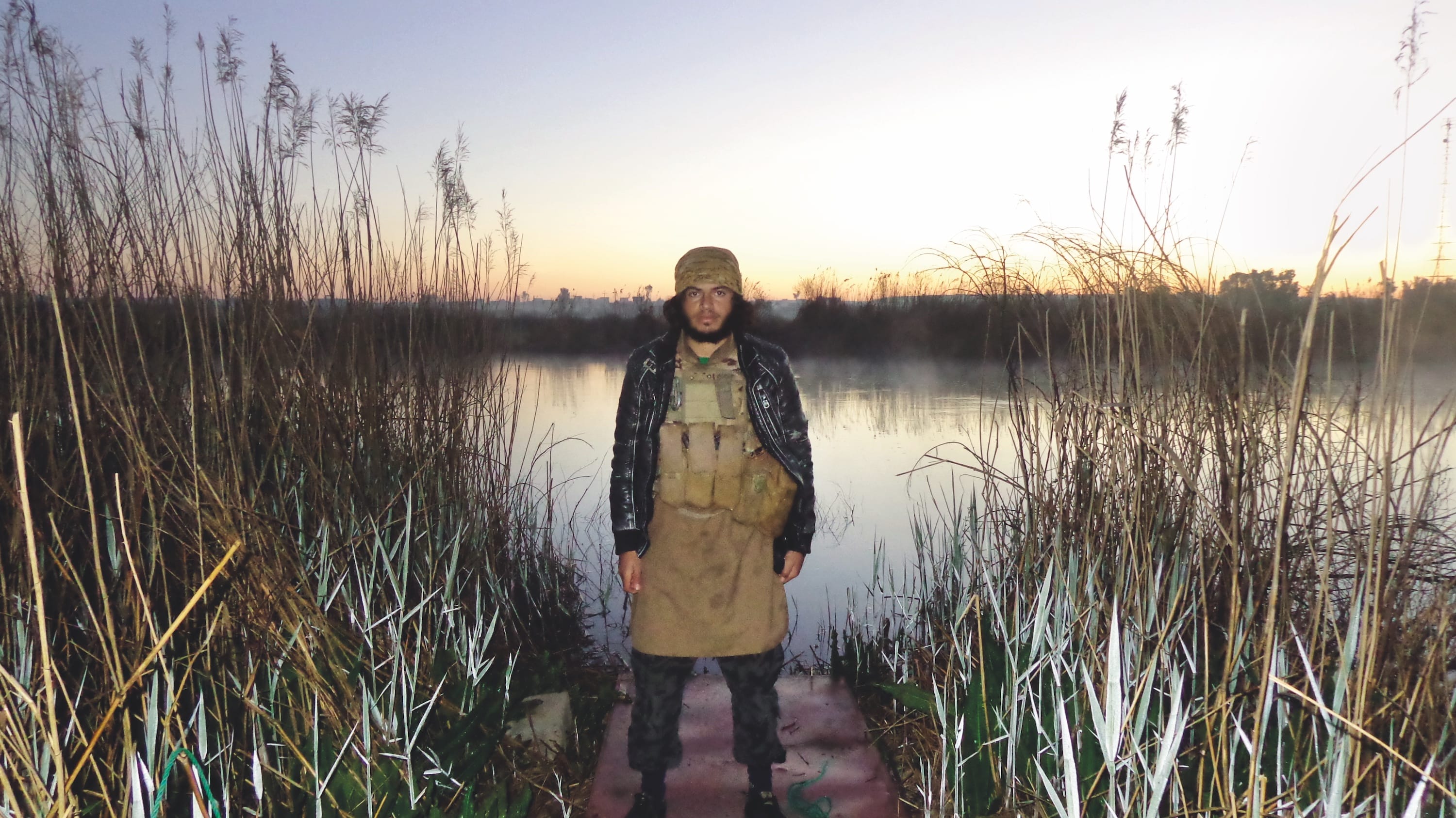 Iraqi man standing in front of a lake wearing a military belt