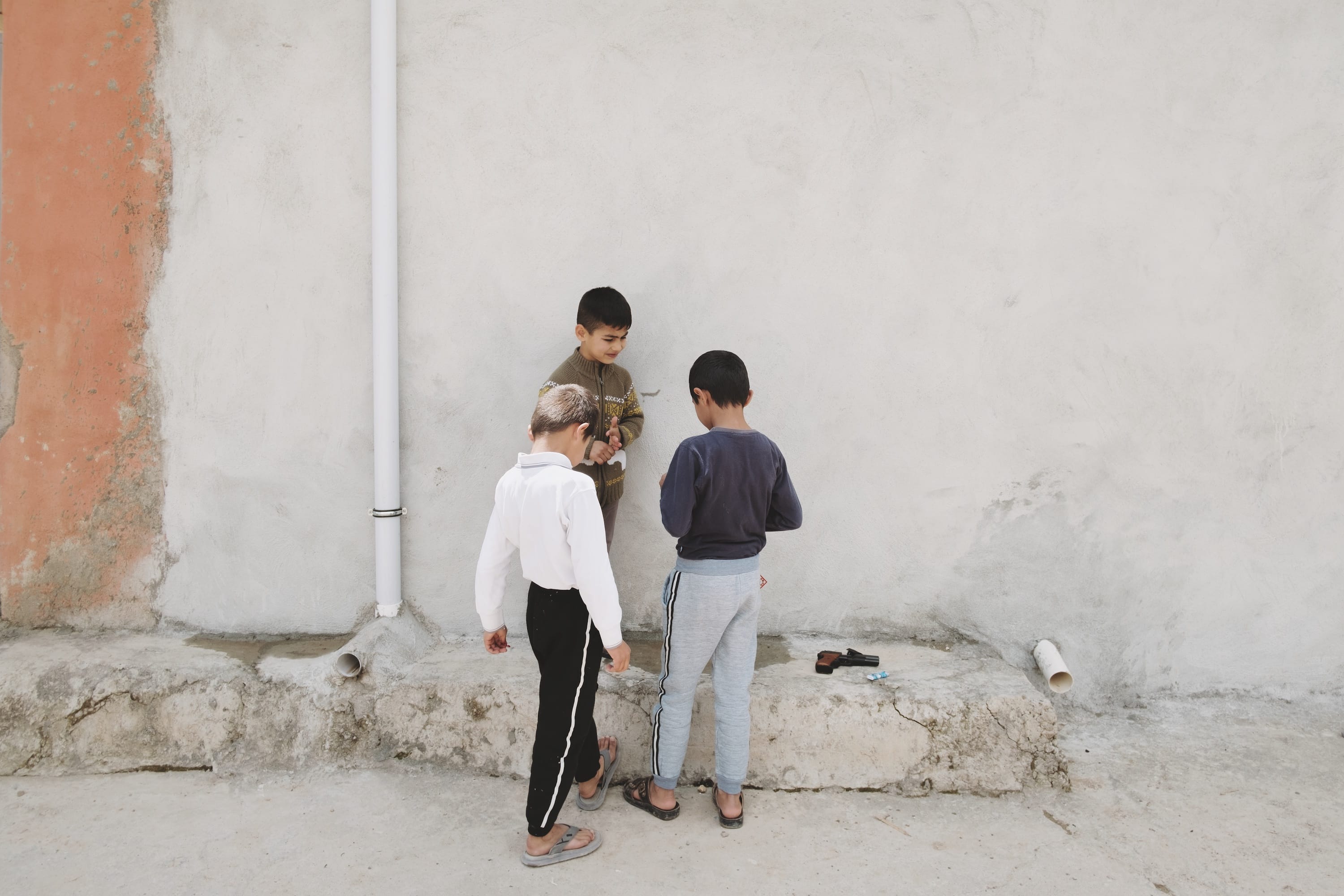 Three little boys, hanging / playing in front of a grey wall.